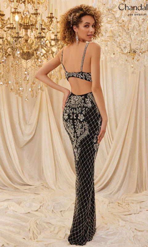 A woman poses in the Long Prom Dress 30123 by Chandalier, a fitted black formal gown with an open back and silver embroidery, showcasing an elegant silhouette amid draped fabric and chandeliers.